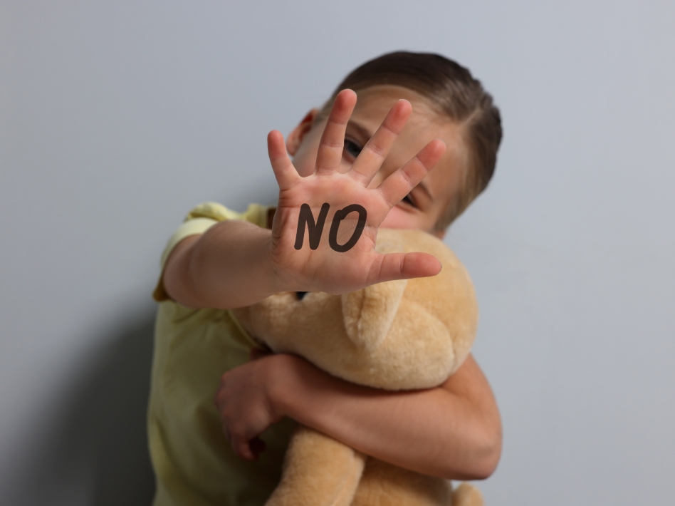 Child holdin stuffed bear while extending one hand with the word 